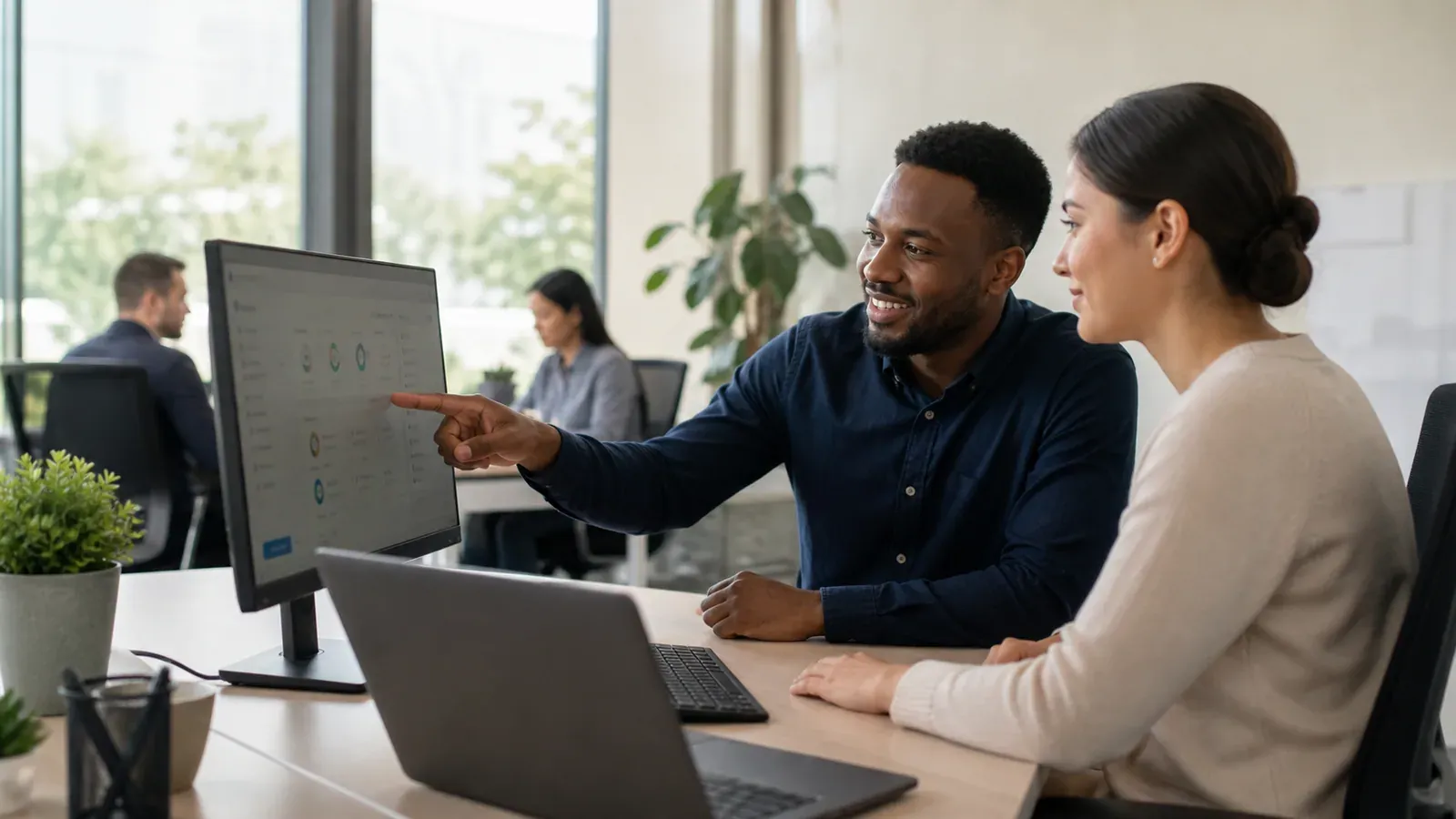 Two coworkers review a desktop monitor together in a bright office